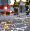 A motorcycle sits next to shattered glass while a firetruck and firefighters are seen in the background.
