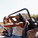 Two women in a convertible SUV drive down a road on a bright, sunny day.