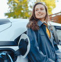 A woman leans against her electric car while it&#x27;s being charged.