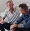 Older father sitting on couch having a serious conversation with his adult son