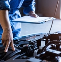 mechanic with a clipboard checking a car engine