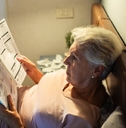 Worried senior woman reading bills in bed at night 