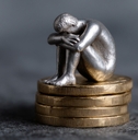 sad person silver figure sits atop of coins