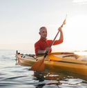 Senior man paddling kayak during sunset