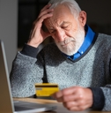 senior man looking worried while holding credit card