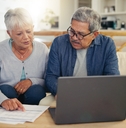 elderly couple using laptop with documents