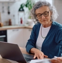 senior woman analyzing documents while using laptop