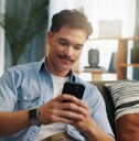 Man playing on phone sitting on couch while smiling slightly