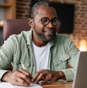 Man taking notes sitting at the desk looking at laptop