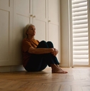 Sad Senior Woman Sitting On Floor At Home 