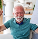 Older man happy smiling with arms up holding a paper
