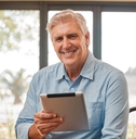 Man in his 60s smiling at the camera holding a tablet
