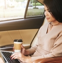 Woman using laptop computer in car while holding a to-go coffee cup