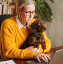 Woman sitting on a desk working from home holding her dog