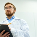 Man wearing lab coat taking notes 