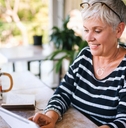Woman with short, white hair sitting at the table reading a letter and having coffee