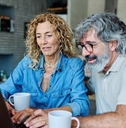 Couple in their 60s sitting at home having coffee and looking at notebook