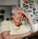 Portrait of worried senior woman sitting in kitchen. 