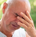Man in his sixties looking worried with eyes closed and hand on his face