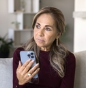 Mature woman holding phone on couch