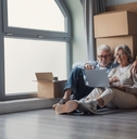 Older couple sitting against moving boxes with laptop