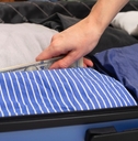 Hand putting cash inside suitcase with clothes