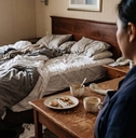 Over the shoulder view of a hotel maid looking at a very messy and dirty hotel room
