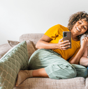 Young couple sitting on couch looking at phone and laptop