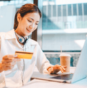 Gen Z woman at cafe on laptop wth debit card in hand