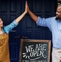 cheerful business owners standing with open blackboard