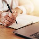 senior person writing notes and using laptop for planning