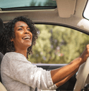 A woman grips the steering wheel and smiles while driving her car.