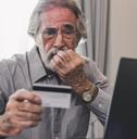upset senior man holding credit card