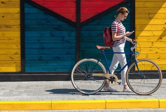 Woman walking her bike along sidewalk, looking down at phone