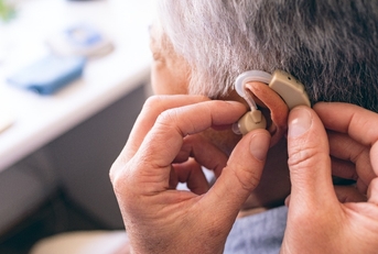 male doctor applying hearing aid to senior woman