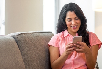 smiling Hispanic woman using her phone at home