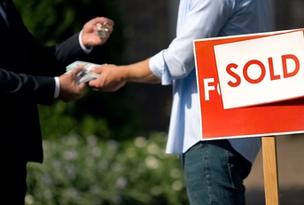 People shaking hands by &#x27;sold&#x27; house sign