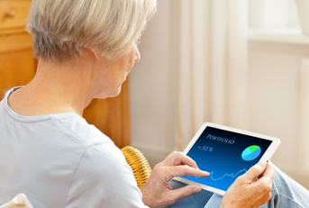 senior woman in her living room checking her investment portfolio on a tablet