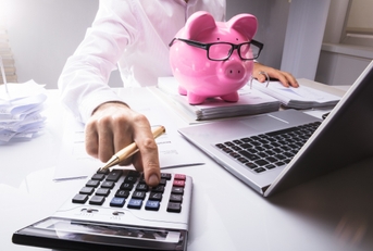 person calculating in front of a piggy bank and a laptop