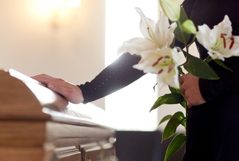 woman with lily flowers and coffin at funeral