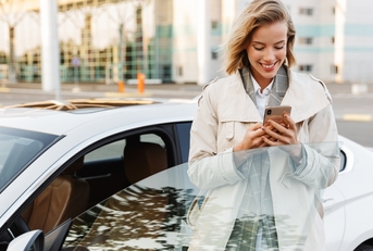 adult woman exiting her car while looking at her phone