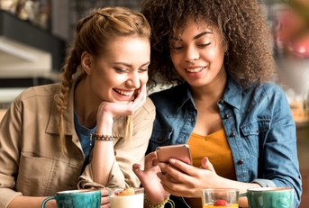 two women smiling and happy while looking at a phone