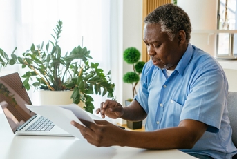 man sitting in his home office with bills in hands