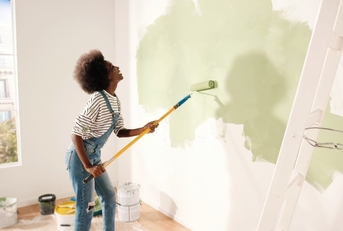 woman dancing and painting wall with roller brush 