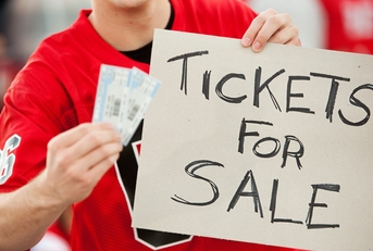 A sports fan holds two tickets and a sign that says &quot;Tickets for Sale.&quot;