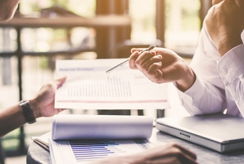 Two men looking at paper financial reports on a table
