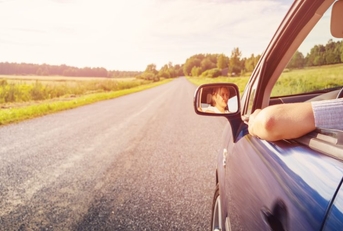 A woman drives down a country road with her arm out the window. 