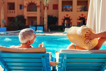 senior couple relaxing on chaise lounges besides a pool