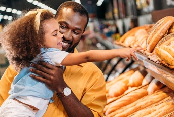 little child pointing by finger at pastry to father in supermarket