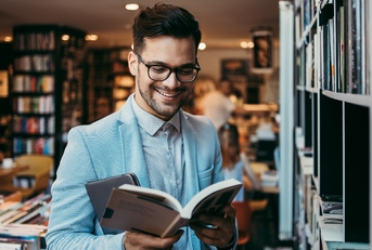 man choosing and reading books in modern bookstore